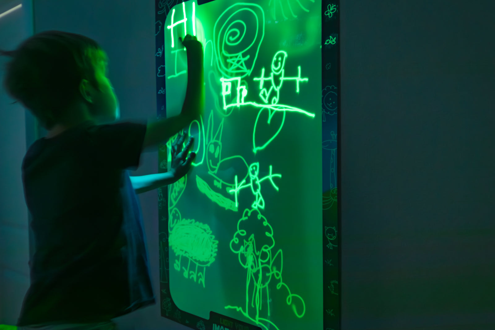 Boy drawing on Glowscape in the dark with various doodles glowing green